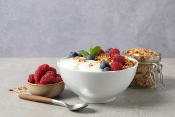 Tasty granola with berries and yogurt in bowl on grey textured table, closeup