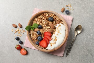 Tasty granola with berries, almond and yogurt served on grey textured table, flat lay
