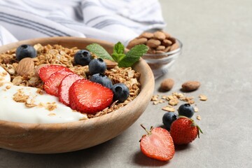 Tasty granola with berries, almond and yogurt in bowl on grey textured table, closeup