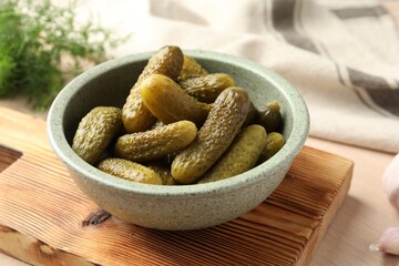 Pickled cucumbers in bowl on wooden table, closeup