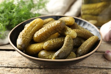 Pickled cucumbers in bowl on wooden table, closeup