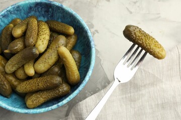 Fork with pickled cucumber and bowl full of ones on grey textured table, top view