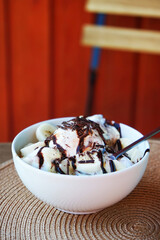 Banana ice cream with chocolate sauce and sliced ​​bananas in a white plate in a street cafe