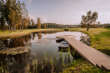 Blome, Latvia - September 11, 2023 -Wooden dock with a rowboat on a calm pond with lily pads,...