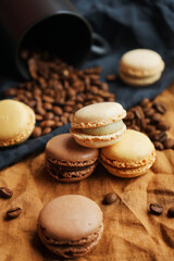 Coffee beans next to a black cup and macarons on linen black and brown towels on a dark background