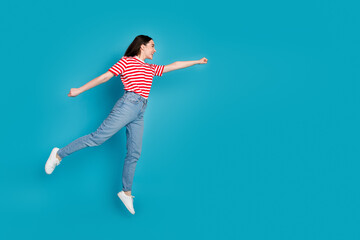 Full length photo of adorable lovely girl wear striped t-shirt jumping high hurrying empty space isolated blue color background