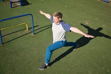 A focused young athlete dynamically performing warm-up drills and stretches outdoors. Clad in...