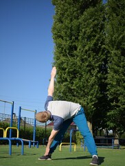 A focused young athlete dynamically performing warm-up drills and stretches outdoors. Clad in...