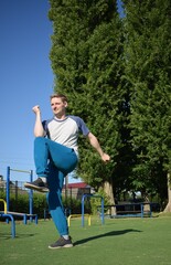 A focused young athlete dynamically performing warm-up drills and stretches outdoors. Clad in...