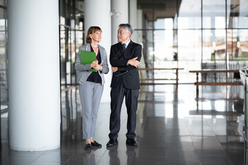 Business meeting. Mature Asian CEO boss and Caucasian executive secretary standing in modern office discussing corporate strategy or financial planning. Diverse people successful working together.