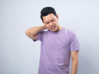 Young Asian man in a lavender t-shirt grimacing and holding his neck, indicating pain or discomfort. Studio shot on a plain background, highlighting his expression and casual fashion.