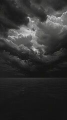 Obraz premium A black and white photograph of a stormy sky over a calm sea at dusk. The clouds are dark and ominous, but the sea is still and peaceful