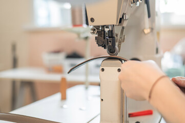 A woman tanner sews a leather belt on a sewing machine. Close-up of hands.