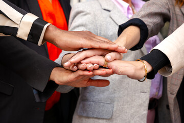 Unrecognizable close-up of diverse businesswomen clasping hands outdoors.