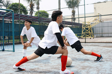 Group Of Young Asian Men Stretching Legs Doing Warm Up Before Playing Football On Outdoor Court