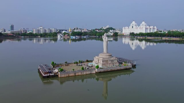 aerial view of buddha statue with telangana secretariate and ambedkar statue in the background with reflections in hussain sagar lake, hyderabad, telangana, india, 4k drone orbit shot