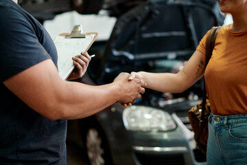 Handshake, deal and woman with mechanic in workshop for contract on vehicle repair or maintenance. Clipboard, agreement and female person shaking hands with industry worker in garage for car service.