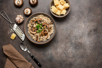 Risotto with mushrooms in a bowl and ingredients on a dark brown grunge background. Top view, flat lay, copy space.
