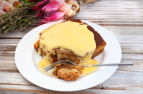 Traditional South African Malva pudding with a bite out. one serving on a plate with burlap and copy space Protea flowers in background