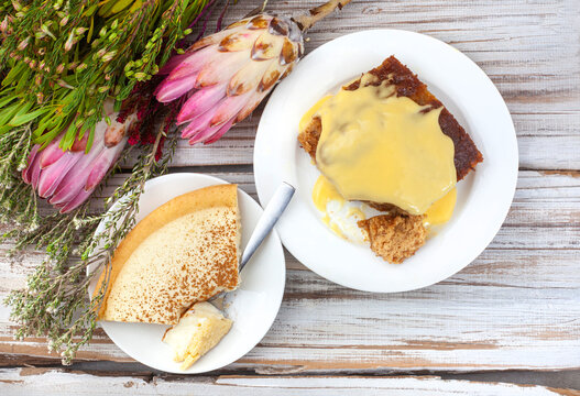 South African dessert favorites, Milk tart and Malva pudding. Flat lay on rustic wood with protea flowers and fynbos. With copy space