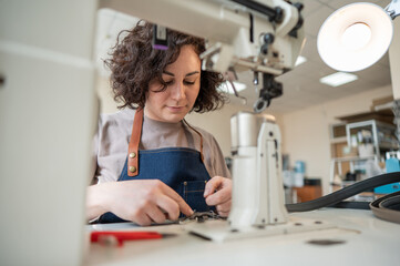 A woman tanner sews a leather belt on a sewing machine. 
