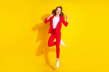 Full body portrait of gorgeous young lady jump raise fists wear red suit isolated on yellow color background