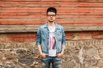 Handsome fashion hipster man with glasses and a cap in trendy denim clothes with a jacket and jeans...