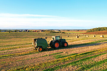Obraz premium Hay making in field. Tractor with round baler. Making Hay Bales in agricultural field. Round Hay Bale Tractor Baler. Balers to roll. High-quality square bales. Baler making Hay Bales in Farm field.