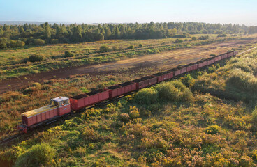 Freight Train transports peat on narrow-gauge, Aerial view. Locomotive with Freight wagons at peat...