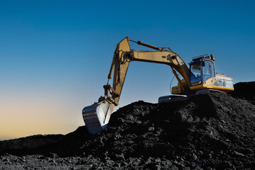 Coal mining in an open pit. Mining excavator loads coal in haul truck in quarry. Excavator digging in open pit coal mine. Excavator in open-pit on sunset background. Heavy machinery in opencast. 