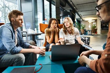 Multicultural business colleagues in casual attire work on laptop and collaborate around a table in...