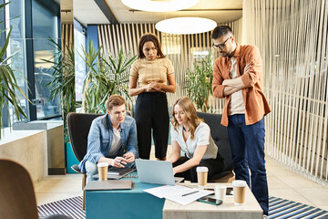 A diverse group of colleagues with laptops engage in a lively discussion around a table, showcasing modern business practices.