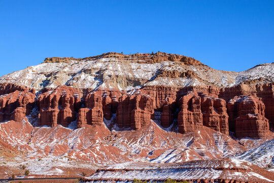 Scenic winter view of snow-dusted red rock formations in Capitol Reef National Park, Utah. A majestic contrast of the white snow with red cliffs under a clear blue sky - USA - Powered by Adobe