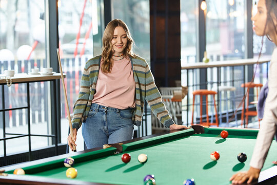 Two women, colleagues in a coworking space, engage in a friendly game of pool, showcasing teamwork and modern business lifestyle.