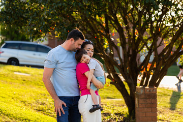 Family by mailbox of home in suburban area of town hugging together