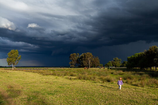 Incoming dark stormy rain clouds over sunlit rural farm paddock with country kid exploring