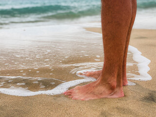 Stopy mężczyzny chodzącego po piasku i falach morskich. Mężczyzna spacerujący boso po plaży. 