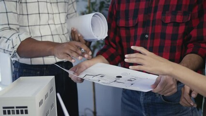 Architects collaborate on blueprints and discuss design plans with a model prototype. Professional consultation and brainstorming session