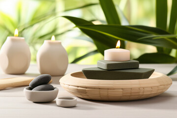 Tranquil composition of lit candles and smooth stones on a wooden table evokes a serene spa ambiance.