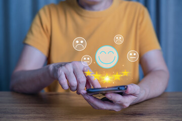 Woman hand touch on smart phone screen to show the smile face emoticon and give five star symbol to...