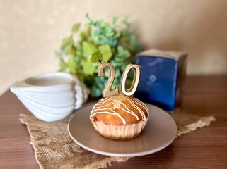 still life with a festive round miniature pie on a plate with candles in the form of the number 20 on a porcelain plate on a wooden table with a linen napkin, gifts and a bouquet of flowers, happy bir