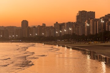 People walking on the beach at golden hour. Sunset in Santos city, Brazil. Waterfront buildings in...