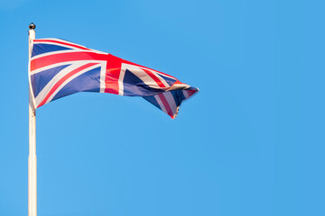 Union Jack flag soars against backdrop clear blue sky, United Kingdom's heritage, resilience, and unwavering spirit