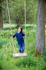 Sweet child, preteen boy, swinging on a wooden swing