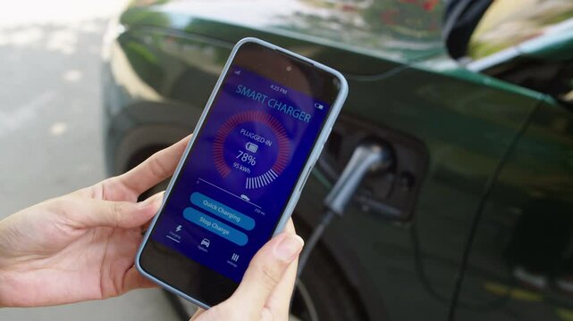 Close up of hands of unrecognizable woman checking charging electric vehicle application on mobile phone while recharging car outdoors