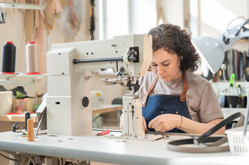 A woman tanner sews a leather belt on a sewing machine. 