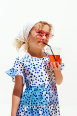 Young dreaming girl dressed summer dress drinking refreshing lemonade in hot summer day against white studio background. Concept of hot summer holidays, vacation, camps, recreation.