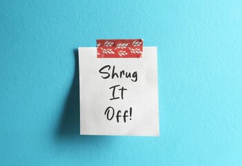 Note stick on blue wall with handwritten text SHRUG IT OFF, concept of to ignore toxic people who never support, stop caring for negative people who despite your wishes