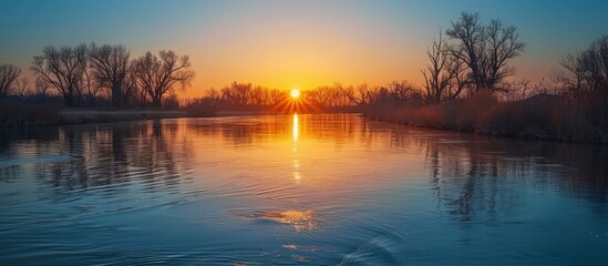 Fototapeta premium Tranquil Sunset Over Serene River with Reflective Water and Bare Trees in Winter Landscape