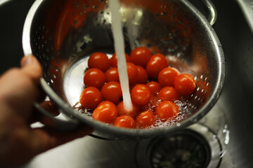 Washing Fresh Cherry Tomatoes in Colander with Running Water in Kitchen Sink